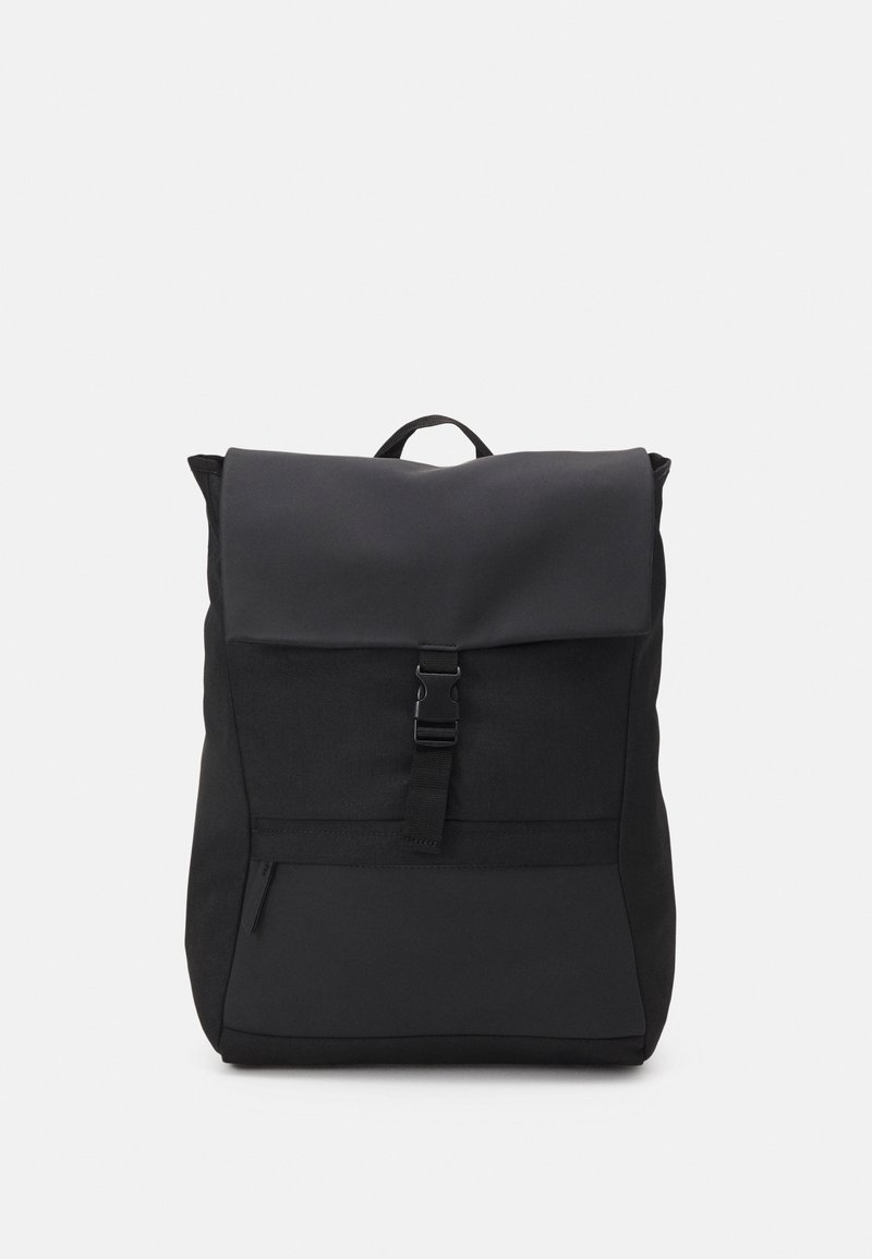 Sac à dos noir avec rabat supérieur, fermeture par boucle, poche avant zippée et poignée de transport, présenté sur un fond uni clair.