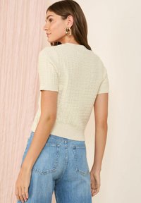 Lichtcrème trui met korte mouwen en gestructureerd breiwerk, met geribde manchetten en onderrand, gecombineerd met blauwe high-waisted denim jeans.