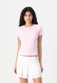Light pink fitted t-shirt with a round neck and short sleeves, paired with a white layered skirt featuring a smocked waistband.