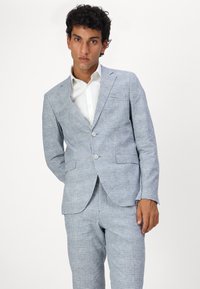 Light blue checked suit with a notched lapel, two buttons, and front pockets. Paired with a white collared shirt. Smooth fabric texture.