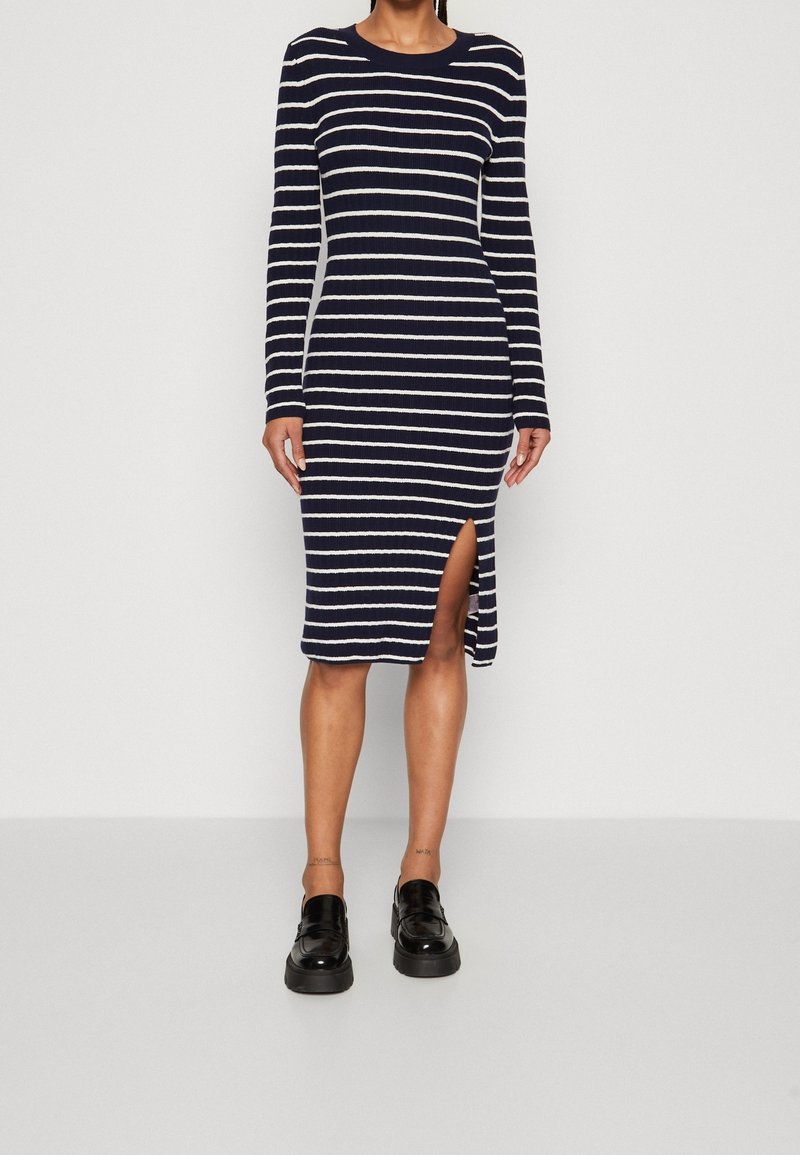 Marinblå randig stickad klänning med långa ärmar, sidssprund och rundad halsringning. Har vita horisontella ränder och ribbad textur.