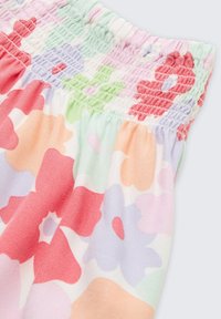Blommönstrad tyg med stora röda, rosa och gröna blommor på en pastellbakgrund. Elastisk smock vid midjan ger struktur.
