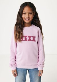 Helles rosa Sweatshirt mit Rundhalsausschnitt und Raglanärmeln, das das Wort "MEXI" in texturierten burgunderfarbenen Buchstaben zeigt. Blaue Jeans.