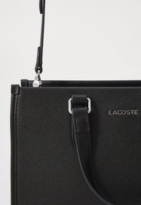 Sac à main en cuir noir avec une surface texturée, quincaillerie en argent et une forme rectangulaire structurée. Comprend une bandoulière détachable.