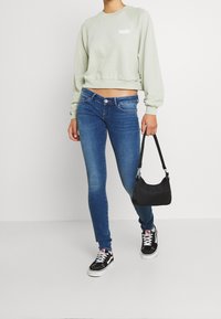 Sweat-shirt court vert menthe avec logo blanc, associé à un jean skinny bleu foncé. Sac à bandoulière noir et baskets noires.