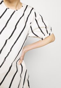 Valkoinen mekko mustilla pystysuorilla raidoilla, lyhyillä puffeilla hihoilla, pyöreällä pääntiellä ja rentolla istuvuudella. Pehmeä materiaali, jolla on sileä rakenne.