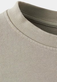Gros plan d'un col rond côtelé beige sur un vêtement en tissu tricoté, montrant les coutures détaillées et la texture.