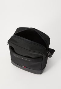 Black crossbody bag made of textured nylon, featuring a zippered main compartment, front pocket, and a striped accent at the bottom.