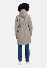 Vaalean beige, puolipitkä takki, jossa on vyötäröön kiristetty malli, huppu ja logoyksityiskohta. Sileä, vettä hylkivä kangas ja pitkät hihat.