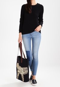 Svart stickad tröja, ljusblå skinny jeans och en svart tygväska med leoparddesign, med bruna handtag och en texturerad yta.