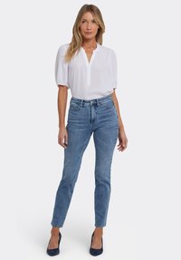 Vit kortärmad blus med knappslå, kombinerad med ljusblå, högmidjade jeans. Modellen bär mörkblå klackar.