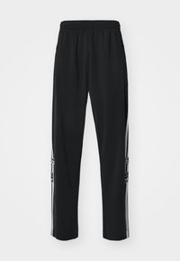 Svarta sportbyxor i mjukt, lätt tyg. Har en dragsko i midjan, avsmalnande ben och vita sidoränder med loggdetalj.