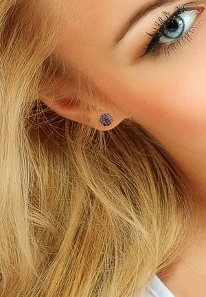 Boucle d'oreille ronde et violette avec une surface texturée, mise en valeur sur des cheveux blonds clairs, soulignant sa couleur et ses détails.