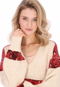Maglione oversize color crema con accenti di paillettes rosse sulle maniche, caratterizzato da un design con scollo a V e tessuto morbido e lavorato a maglia.