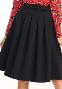 Czarna plisowana spódnica do kolan z szerokim paskiem, w zestawie z czerwoną bluzką w kwiaty z długim rękawem.