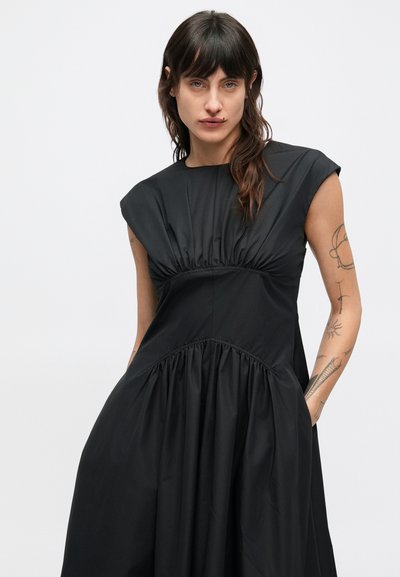 Fekete ruha, testhezálló felsőrésszel, ráncolt derékkal és bővülő szoknyával. Sima anyagból készült, rövid ujjakkal és két oldalzsebbel.