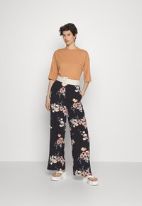 Uma t-shirt oversized combinada com calças largas pretas com padrão floral. As calças apresentam padrões florais coloridos, complementados por um cinto branco e sandálias chunky.