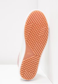 Suela de una zapatilla con una superficie de goma texturizada. Presenta un patrón de rayas diagonales en naranja, bordeado por un lateral blanco.