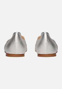 Silberne metallische Ballerinas mit glatter Textur, runder Zehenpartie und einer niedrigen braunen Sohle. Rückansicht, die das klare Design und die minimalistischen Details zeigt.