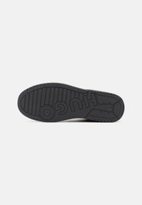 Sort gummisål til sneakers med kontrasterende struktureret grebsmønster, der har det præget logo "HUGO" og karakteristiske riller for bedre traction.