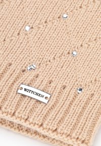 Beige gebreide sjaal met geribbelde textuur, versierd met kleine zilveren studs en een metalen label met de merknaam "WITTCHEN."