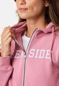 Rosa Zip-Up-Hoodie mit weißem "SEASIDE"-Druck. Verfügt über eine Kapuze mit Kordelzug, metallischen Reißverschluss und gerippte Bündchen. Weiches Stoffgefühl.
