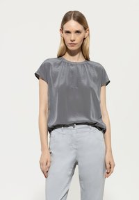 Graues Satin-Top mit kurzen Ärmeln, rundem Ausschnitt und subtilen Falten. Kombiniert mit hellgrauen maßgeschneiderten Hosen. Glatte Textur.