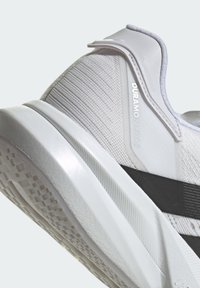 Baskets blanches avec un dessus en maille texturée, accent de semelle intermédiaire noir solide et détail de marque réfléchissant. Semelle extérieure en caoutchouc avec motif de traction.