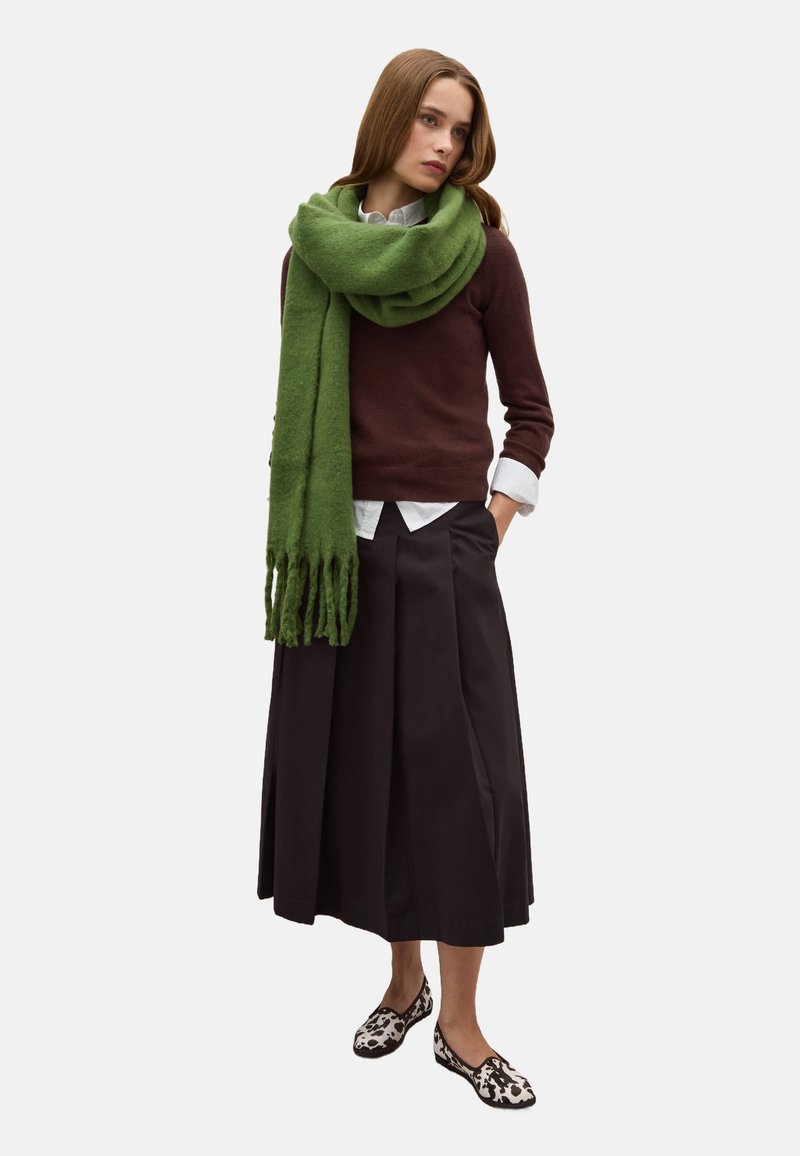 Cardigan marrone, camicia bianca con colletto, sciarpa verde, gonna nera plissettata e ballerine a righe in bianco e nero. Tessuti morbidi, look a strati.