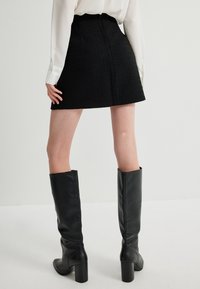 Schwarzer Minirock aus strapazierfähigem Stoff mit ausgestellter Silhouette, kombiniert mit kniehohen Lederstiefeln und einer weißen Bluse.