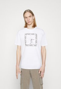 Balta kokvilnas t-krekls ar grafisku dizainu, kurā melnā kr�āsā apzīmēts vārds "PREMIUM" ap rozā zieda kontūru. Īsas piedurknes, apaļa kakla izgriezums.