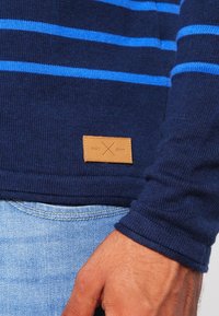 Marineblauer gestrickter Pullover mit horizontalen hellblauen Streifen. Besitzt ein Lederetikett mit "edc X dnm." Zeigt ein tailliertes Design und gerippte Bündchen.