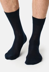 Calcetines de algodón color azul marino con un puño acanalado, textura suave y una longitud estándar de tripulación, mostrando parcialmente los pies y las piernas inferiores.