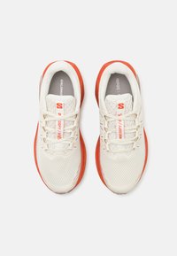 Kremfargede og oransje joggesko har en pustende mesh-overdel, teksturert design, polstret tunge og kontrasterende gummisåle.
