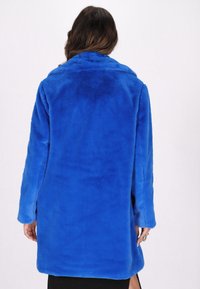 Royal blue, plyssede teksturfrakke med lange ærmer og bred krave. Har en lige pasform og en blød overflade.