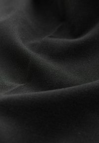 Tessuto nero con una texture liscia e opaca, caratterizzato da pieghe sottili che creano profondità e un aspetto uniforme in tutto il materiale.