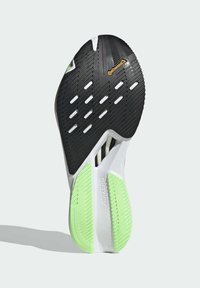 Semelle de sneaker en caoutchouc noir avec des accents verts, présentant des motifs de grip texturés et des découpes pour plus de flexibilité. Marque "ADIZERO" visible.