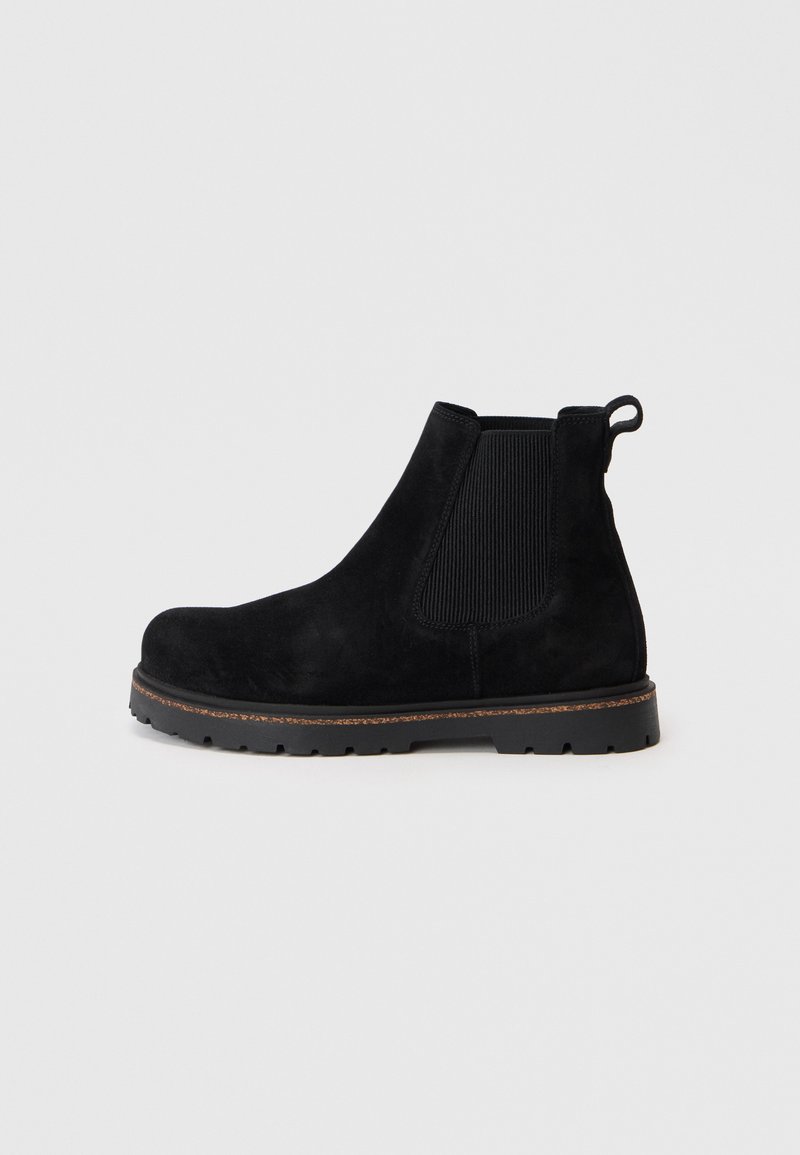 Stivale Chelsea anklet in suede nero con pannello elastico laterale, linguetta sul tallone e suola robusta con rifinitura marrone su sfondo semplice.