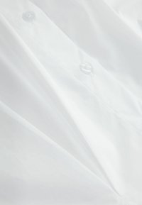 Gros plan d'une chemise blanche avec deux boutons transparents visibles et de légers plis dans le tissu.
