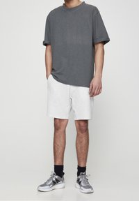 T-shirt gris à manches courtes, shorts gris clair et chaussures de sport grises avec des accents noirs. Tissu lisse et coupe décontractée.