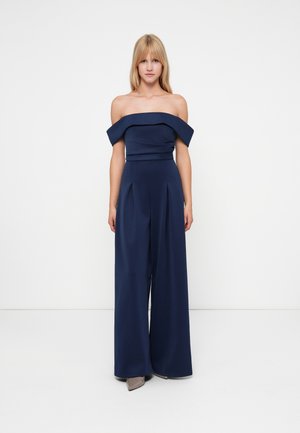 Mono azul marino sin hombros con piernas anchas plisadas, corsé estructurado y textura de tela suave. Diseño simple sin embellecimientos visibles.