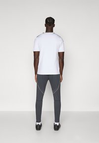 Hvid atletisk t-shirt med korte ærmer, parret med mørkegrå tætsiddende bukser med gule accenter og en tapered design.