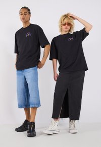 Loose black cotton T-shirts with unique graphic designs, paired with light denim shorts and a black split skirt, complemented by white sneakers.