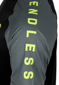 Ropa deportiva negra con una manga texturizada de patrón gris y el atrevido texto amarillo "ENDLESS" a lo largo del costado.