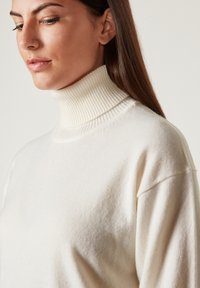 Cremfarbener Rollkragenpullover aus weichem Strickstoff, mit einem gerippten Kragen und lockerer Passform, mit einer glatten Textur.