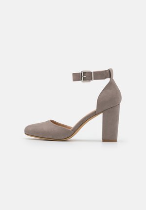 Zapato de salón de ante gris con tacón alto, puntera redondeada, tira en el tobillo con hebilla plateada y tacón grueso de bloque.