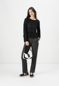 Top nero a maniche lunghe con motivo texturizzato, orlo a peplo, pantaloni grigi sartoriali, borsa bicolore nera e bianca, e sneakers nere con suole in gomma.