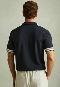 Tricou polo bleumarin cu un finisaj texturat, dotat cu mansete striped alb și gri. Tricoul are un guler standard și o croială lejeră.