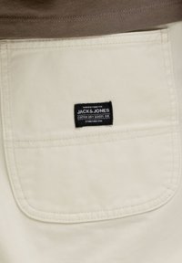 Τσέπη μπεζ παντελονιού με μικρή μαύρη υφασμάτινη ετικέτα που γράφει "Κατασκευασμένο για Jack & Jones Cotton Dry Goods Div. Ιδρύθηκε το 1990."