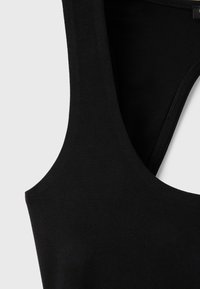 Gros plan d'un vêtement noir sans manches montrant le tissu lisse et les coutures autour des emmanchures et de l'encolure.